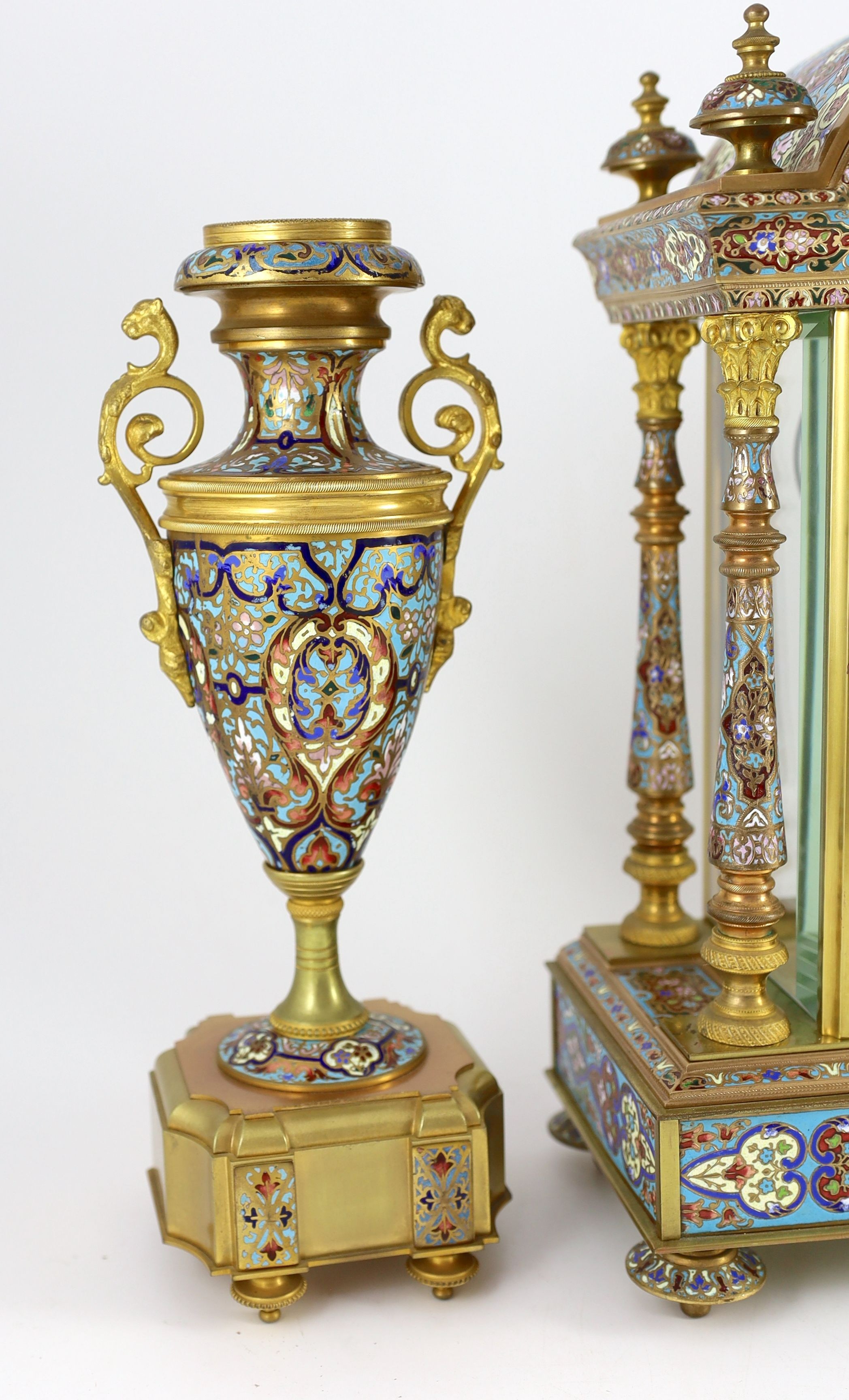 An early 20th century French ormolu and champleve enamel clock garniture, clock: height 50.5cm urns: height 32.5cm